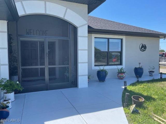 property entrance with roof with shingles and stucco siding