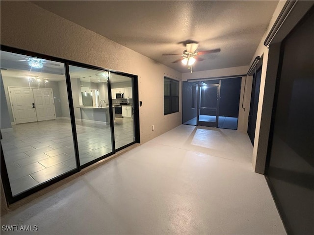 interior space with a ceiling fan, a textured wall, a textured ceiling, concrete flooring, and a sink