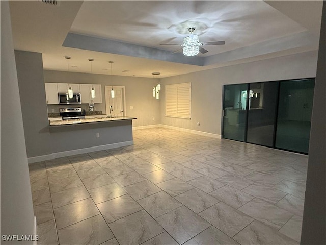 unfurnished living room with a raised ceiling, ceiling fan, marble finish floor, and baseboards