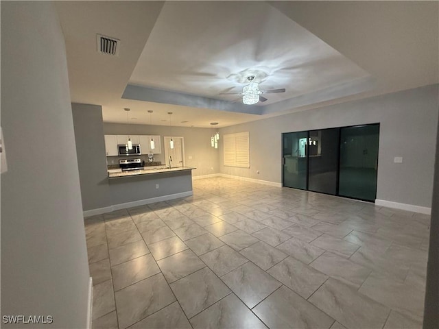 unfurnished living room with a ceiling fan, a tray ceiling, visible vents, and baseboards