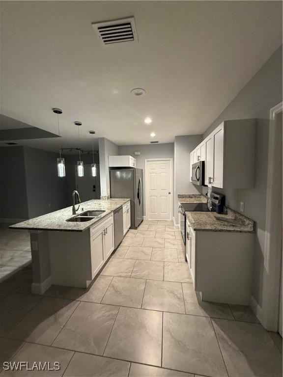 kitchen featuring visible vents, appliances with stainless steel finishes, light stone counters, white cabinetry, and a sink