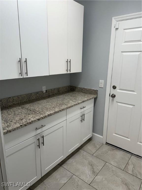 kitchen featuring marble finish floor, baseboards, white cabinetry, and light stone counters