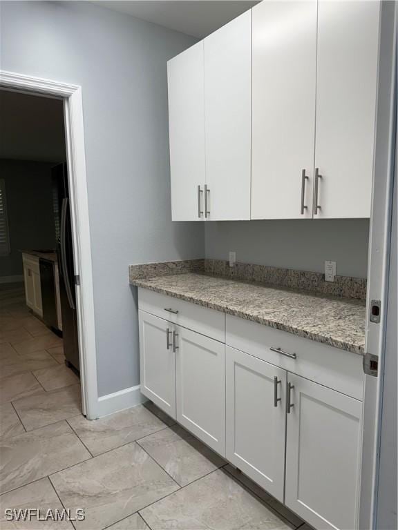 kitchen with baseboards, light stone counters, freestanding refrigerator, and white cabinetry