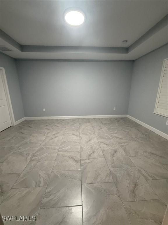 spare room featuring marble finish floor, a raised ceiling, and baseboards