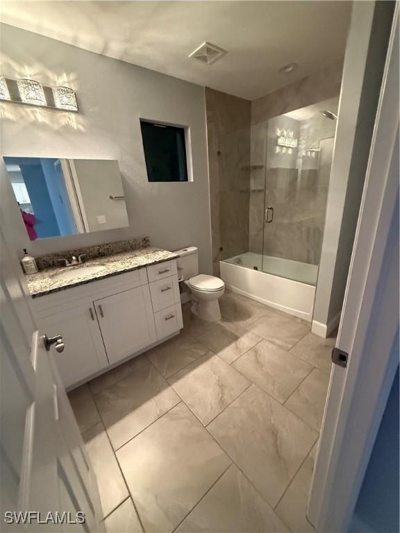 full bathroom featuring marble finish floor, shower / bath combination with glass door, visible vents, toilet, and vanity