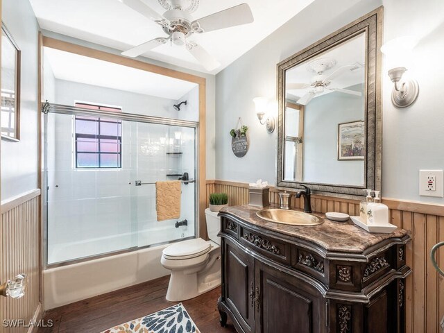 full bathroom with combined bath / shower with glass door, wood walls, wood-type flooring, vanity, and toilet