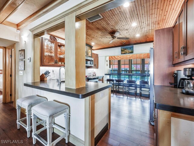 kitchen with appliances with stainless steel finishes, a kitchen breakfast bar, dark hardwood / wood-style floors, wooden ceiling, and kitchen peninsula