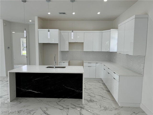 kitchen with an island with sink, white cabinetry, sink, and pendant lighting