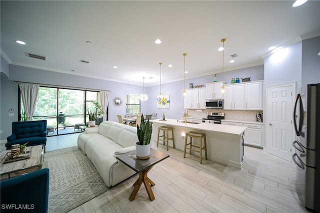 living room with a notable chandelier, sink, crown molding, and light hardwood / wood-style flooring