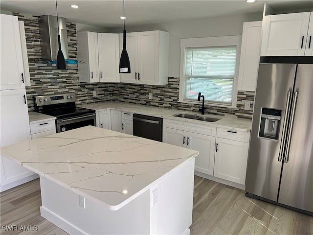 kitchen featuring wall chimney range hood, sink, hanging light fixtures, stainless steel appliances, and white cabinets