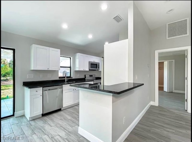 kitchen featuring kitchen peninsula, appliances with stainless steel finishes, white cabinets, and light hardwood / wood-style flooring