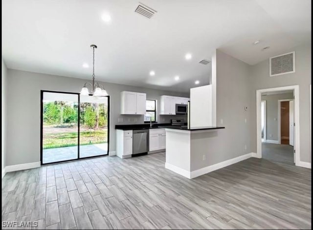 kitchen with decorative light fixtures, light wood-type flooring, white cabinetry, and appliances with stainless steel finishes