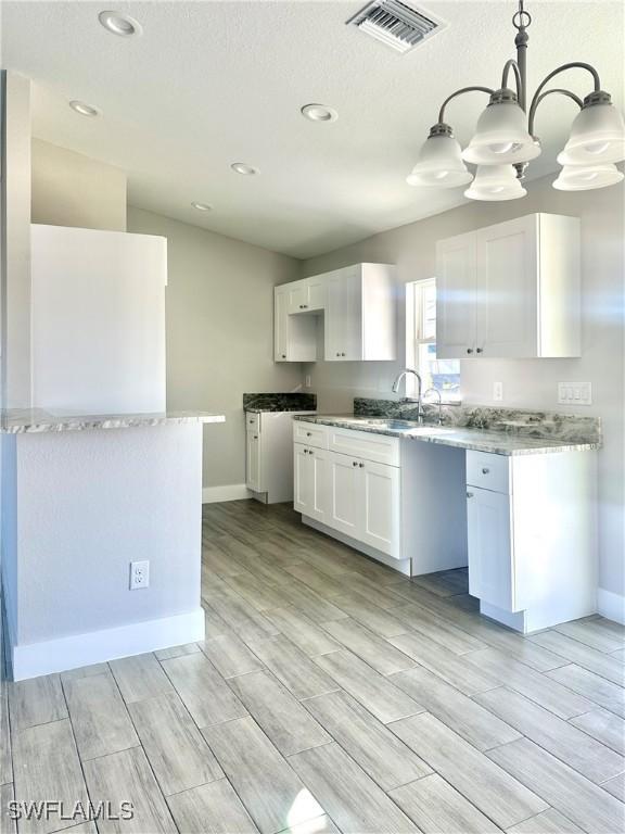 kitchen with sink, decorative light fixtures, white cabinetry, and light hardwood / wood-style flooring