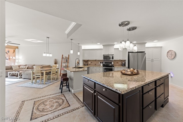 kitchen with appliances with stainless steel finishes, a kitchen island, sink, decorative light fixtures, and white cabinetry