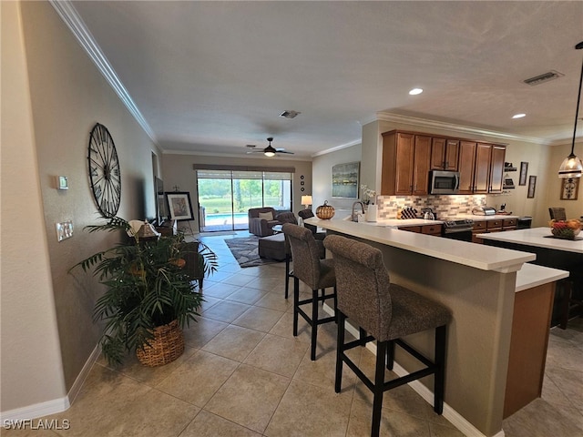 kitchen featuring kitchen peninsula, ceiling fan, appliances with stainless steel finishes, a breakfast bar, and crown molding