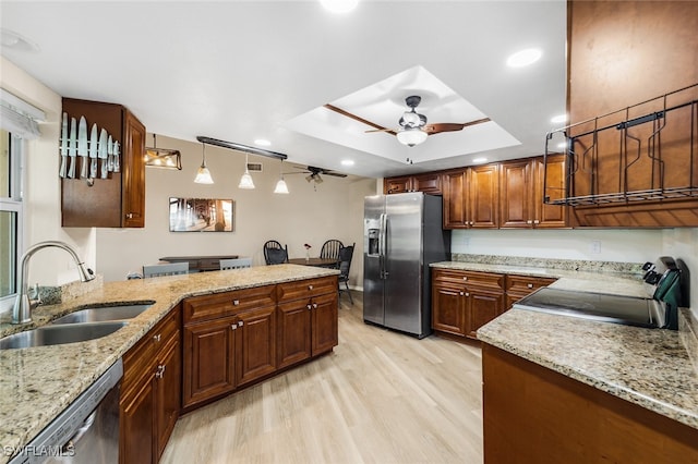 kitchen with light wood-type flooring, stainless steel appliances, a raised ceiling, sink, and decorative light fixtures