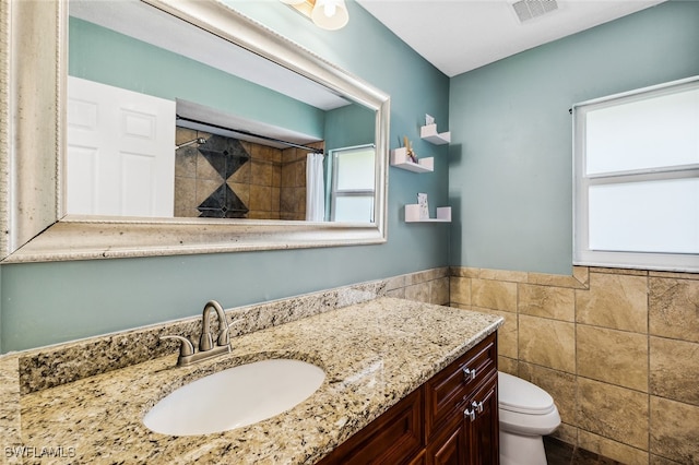 bathroom featuring a shower with shower curtain, vanity, toilet, and tile walls