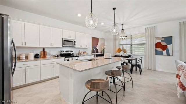 kitchen with a kitchen island with sink, decorative light fixtures, stainless steel appliances, and white cabinetry