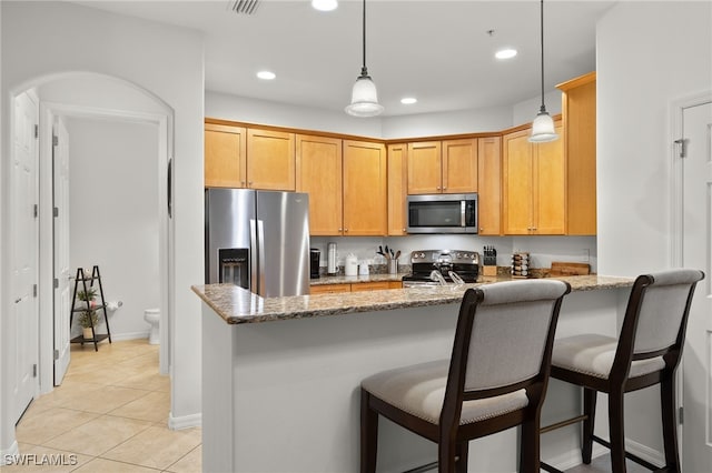 kitchen with appliances with stainless steel finishes, kitchen peninsula, light stone counters, and pendant lighting