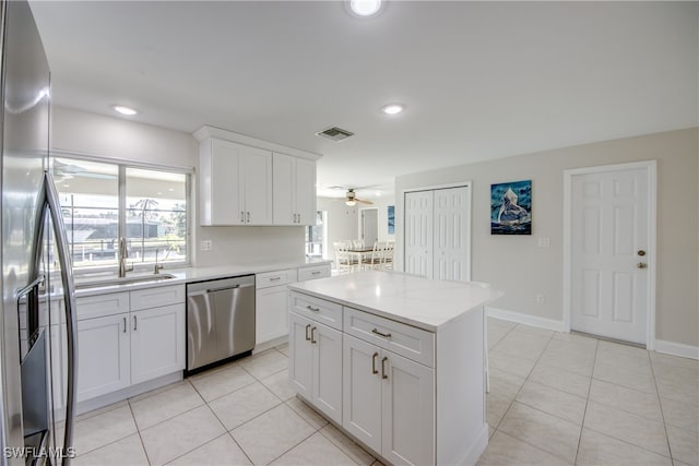 kitchen with sink, a center island, stainless steel appliances, white cabinets, and light tile patterned floors