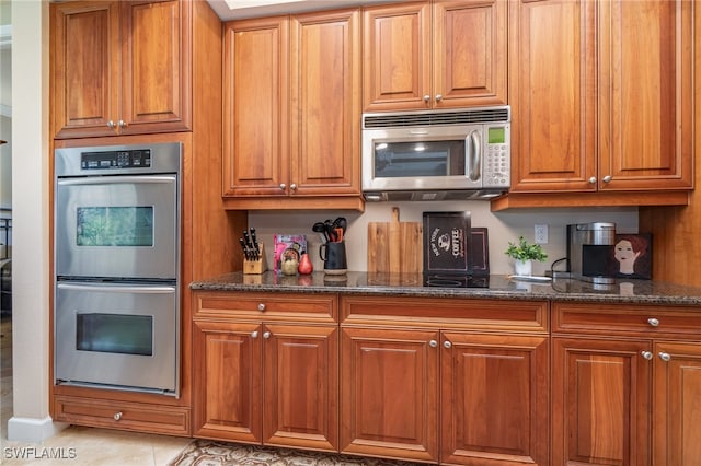 kitchen featuring light tile patterned floors, dark stone counters, and appliances with stainless steel finishes