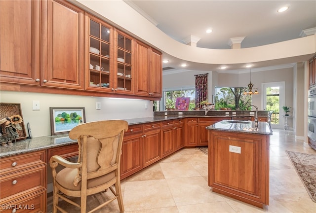 kitchen featuring a center island with sink, decorative light fixtures, dark stone countertops, and ornamental molding