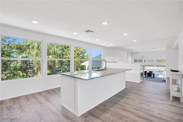 kitchen featuring light stone counters, light wood-style flooring, a sink, visible vents, and a center island with sink