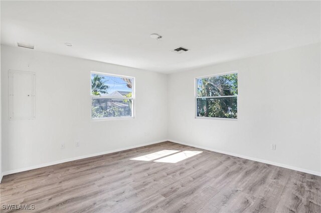 empty room with light wood-type flooring, baseboards, electric panel, and visible vents