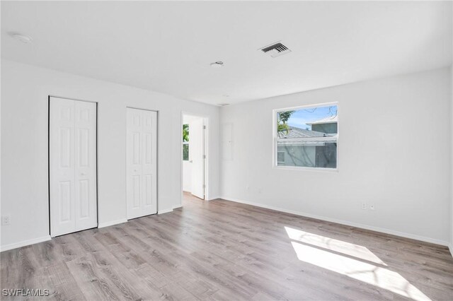 unfurnished bedroom with light wood-style flooring, two closets, visible vents, and baseboards