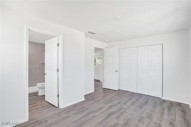 unfurnished bedroom featuring light wood-type flooring, attic access, visible vents, and baseboards