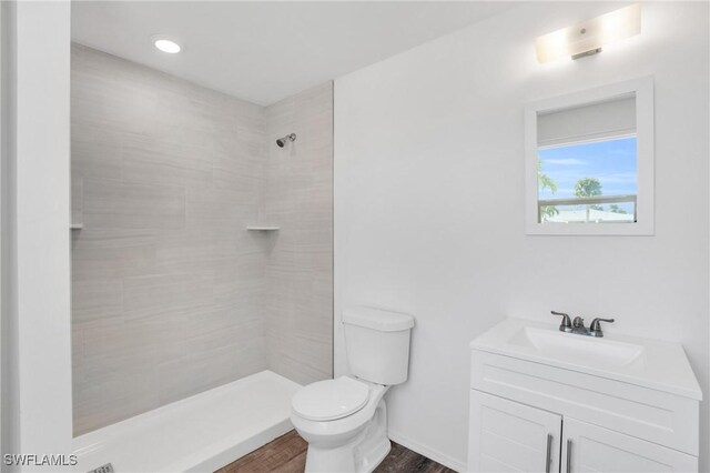 full bath featuring baseboards, toilet, wood finished floors, a tile shower, and vanity