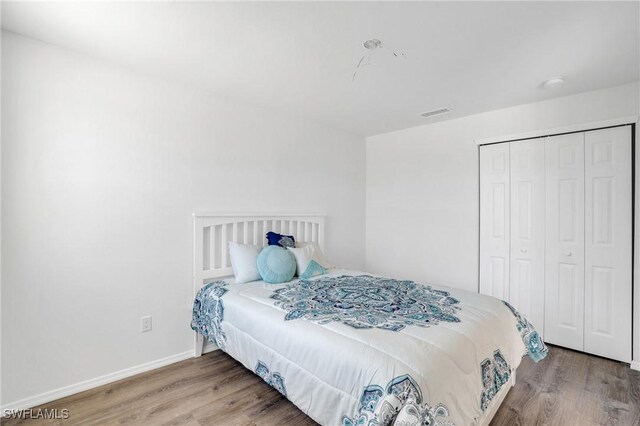 bedroom with a closet, wood finished floors, visible vents, and baseboards