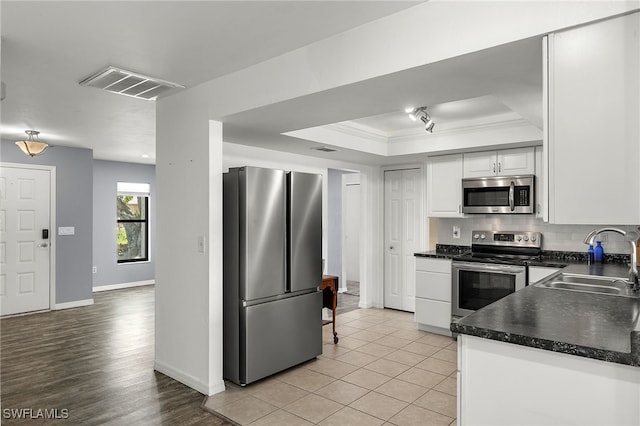 kitchen with stainless steel appliances, white cabinetry, sink, a tray ceiling, and crown molding