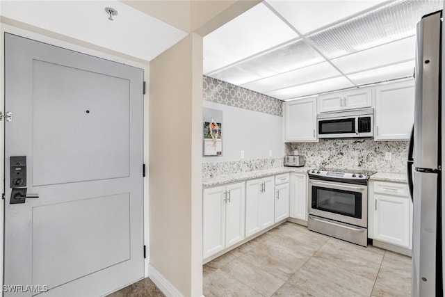 kitchen with decorative backsplash, stainless steel appliances, light stone countertops, and white cabinetry