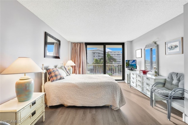 bedroom with access to exterior, light hardwood / wood-style flooring, a textured ceiling, and floor to ceiling windows