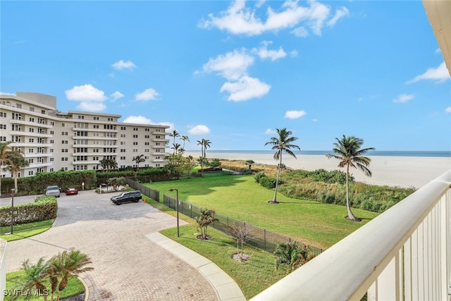 view of community featuring a lawn, a water view, fence, and a view of the beach