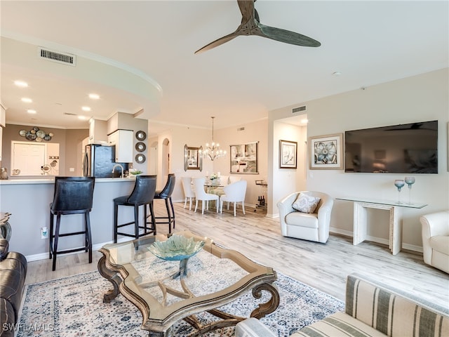 living room with ceiling fan with notable chandelier, ornamental molding, and light hardwood / wood-style flooring