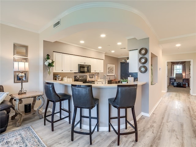 kitchen with stainless steel electric range, kitchen peninsula, ornamental molding, light hardwood / wood-style floors, and white cabinetry