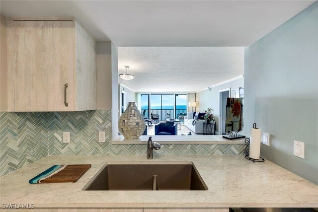 kitchen with backsplash, light brown cabinets, light stone countertops, and sink