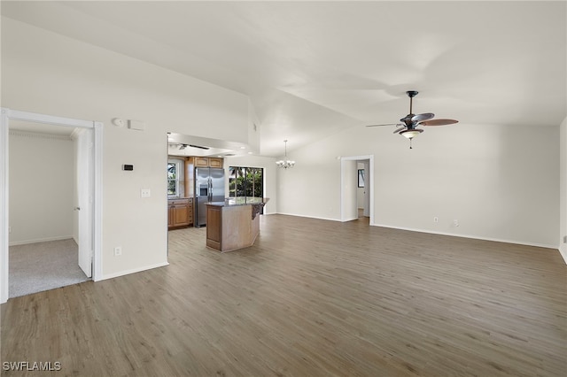 unfurnished living room with lofted ceiling, ceiling fan with notable chandelier, and hardwood / wood-style floors