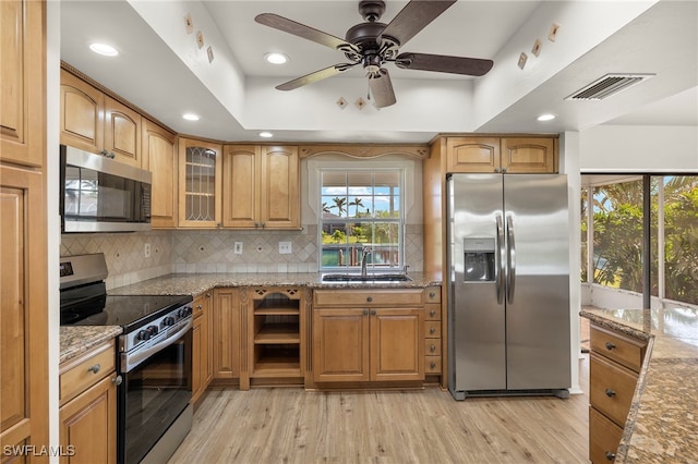 kitchen with a wealth of natural light, appliances with stainless steel finishes, light stone countertops, and light wood-type flooring