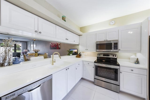 kitchen with kitchen peninsula, light tile patterned floors, appliances with stainless steel finishes, white cabinetry, and sink