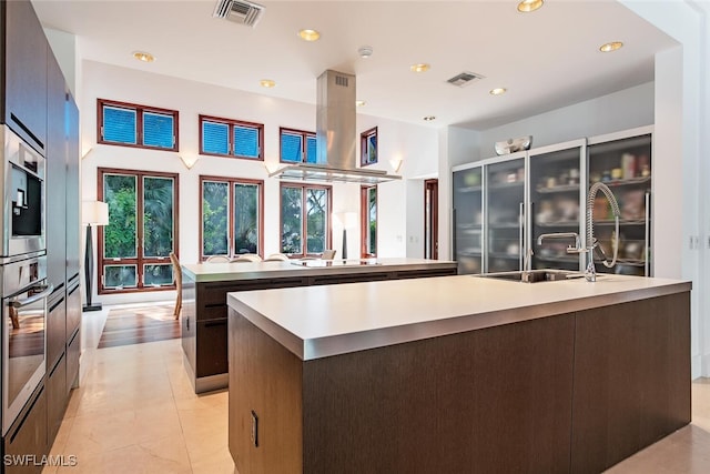 kitchen with stainless steel appliances, dark brown cabinetry, a center island with sink, sink, and light tile patterned floors