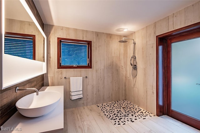 bathroom with hardwood / wood-style floors, wooden walls, sink, and tiled shower