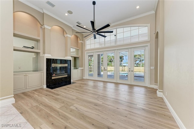 unfurnished living room featuring light hardwood / wood-style floors, french doors, a premium fireplace, and ceiling fan