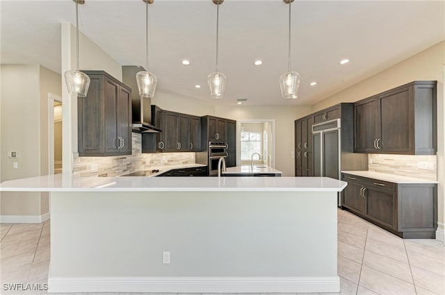 kitchen featuring dark brown cabinetry, pendant lighting, paneled built in fridge, and tasteful backsplash