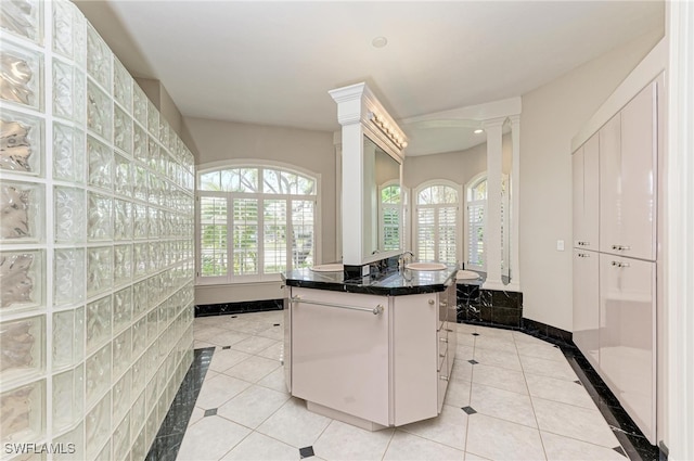 kitchen with a kitchen breakfast bar, white cabinetry, ornate columns, light tile patterned floors, and a center island with sink