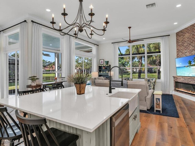 kitchen with decorative light fixtures, a fireplace, ornamental molding, and a center island with sink