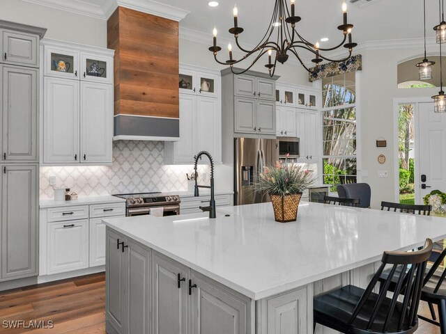 kitchen featuring a breakfast bar, hanging light fixtures, a center island with sink, ornamental molding, and appliances with stainless steel finishes