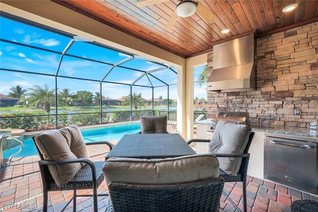 view of patio with area for grilling, an outdoor kitchen, a water view, glass enclosure, and ceiling fan